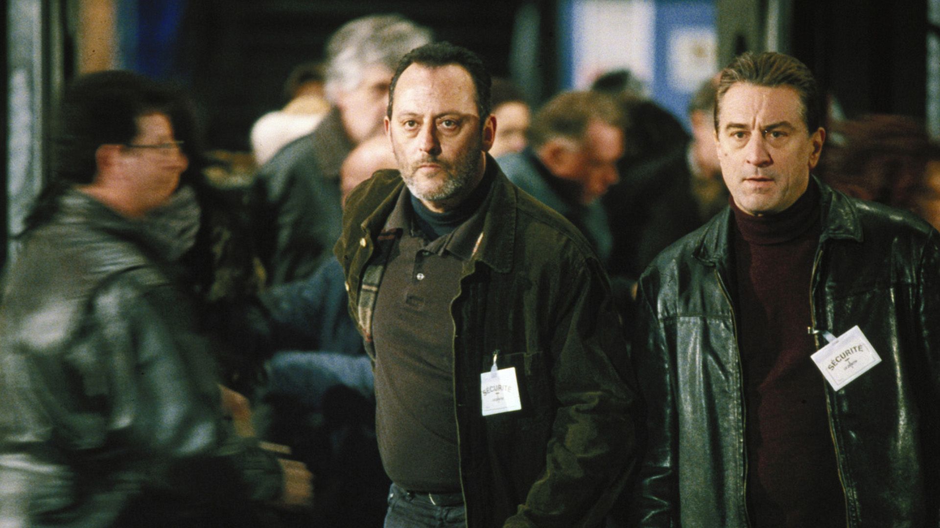 Jean Reno y Robert De Niro de negro con insignias que dicen "seguridad" en sus pechos