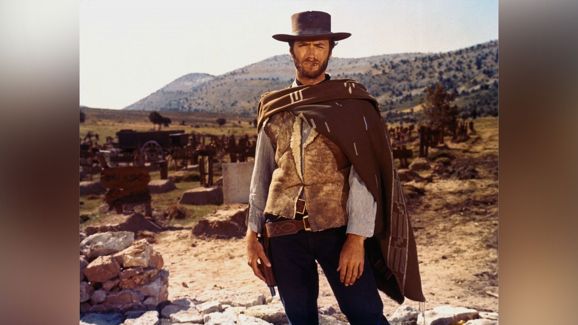 La ambientación del Lejano Oeste, un hombre barbudo con un sombrero de ala ancha y poncho frunce el ceño a la cámara