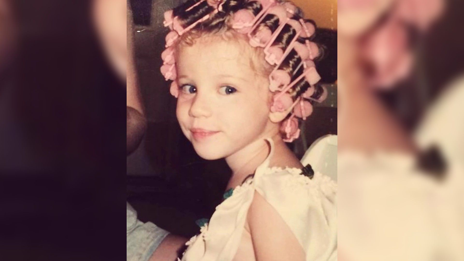 Una niña con un vestido blanco y rulos rosados en el cabello