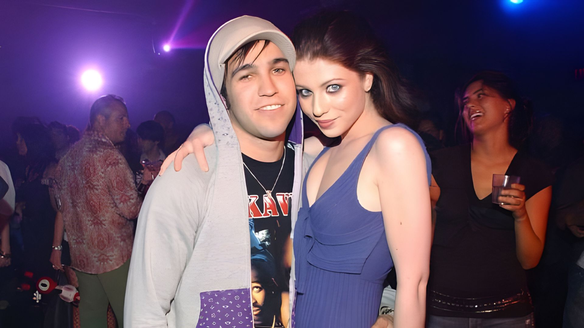 La actriz Michelle Trachtenberg y el músico Pete Wentz se abrazan mientras la gente se divierte de fondo