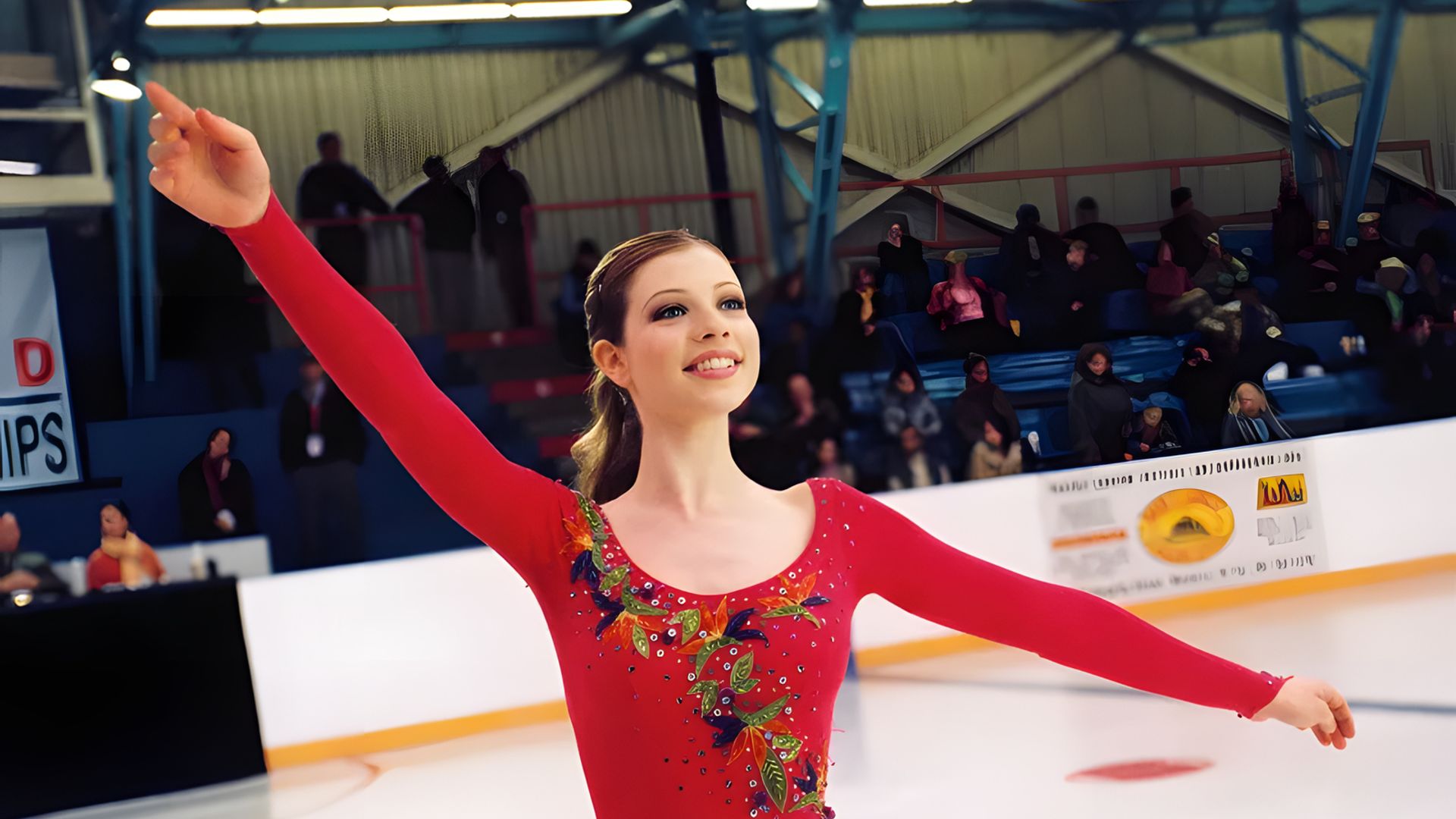 Michelle Trachtenberg en un traje de patinadora rojo baila sobre el hielo, brazos levantados