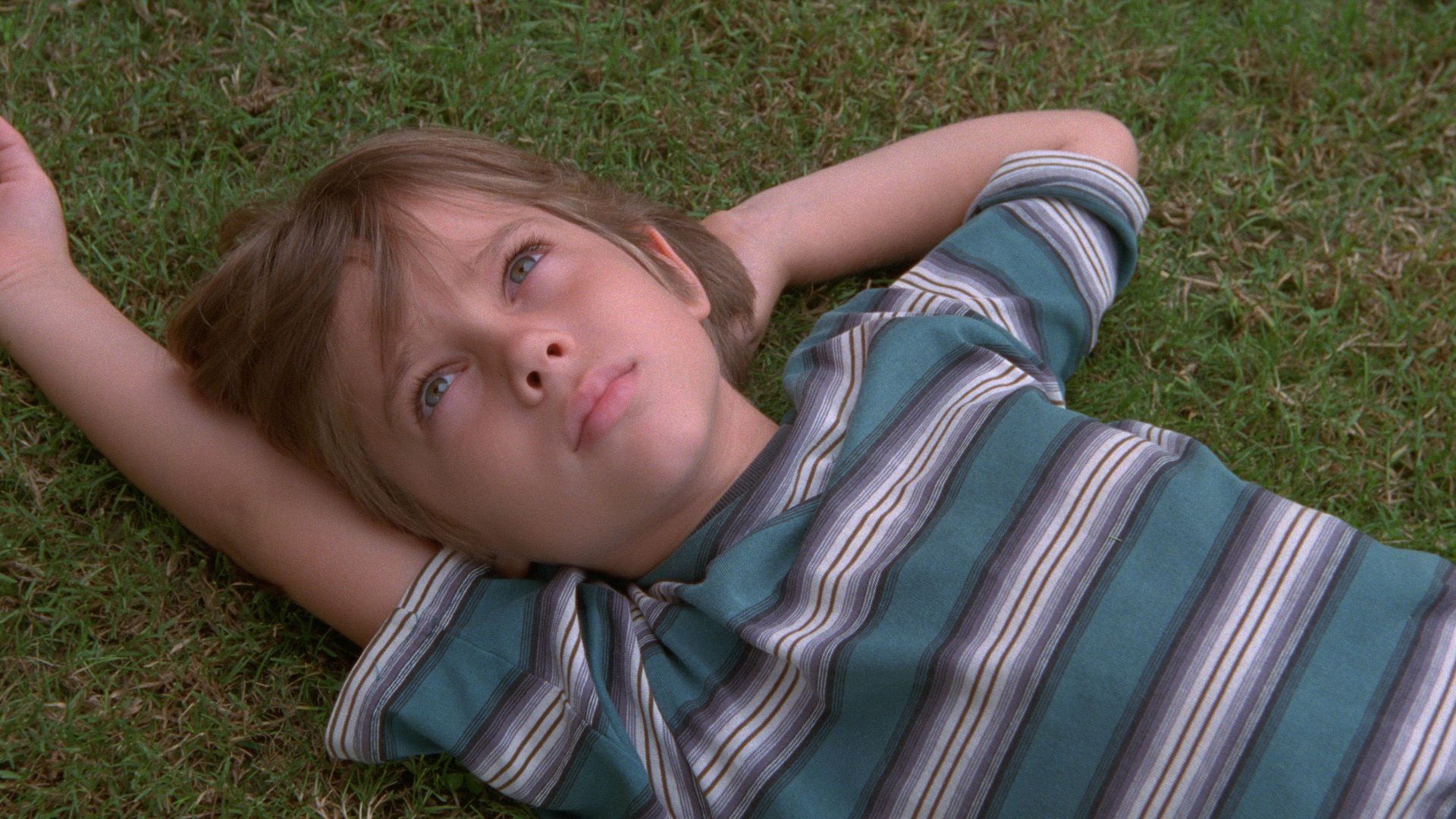 Una imagen de la película "Boyhood": el joven Ellar Coltrane con una camiseta a rayas tumbado en el césped