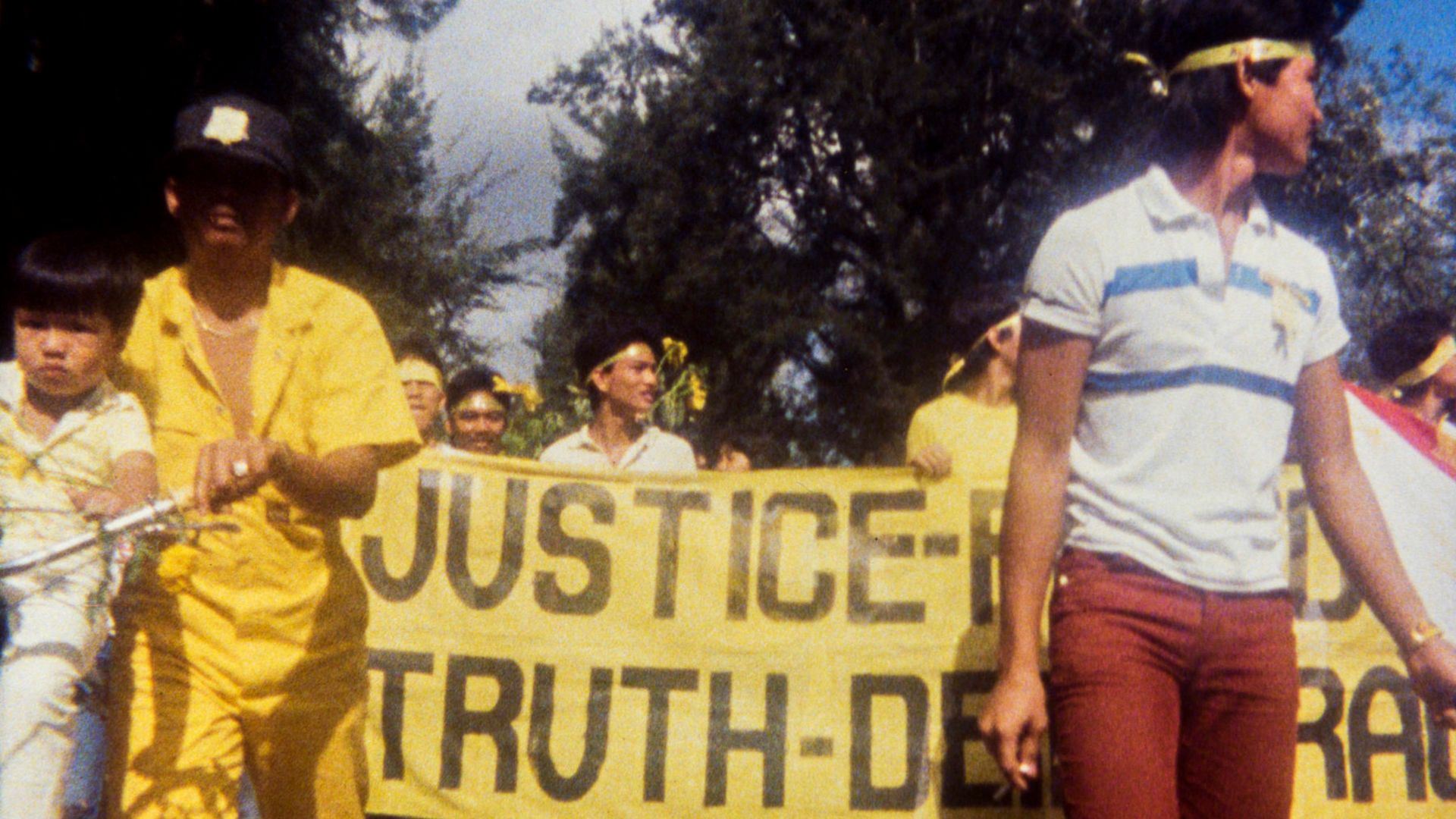 Fotograma de la película "¿Why is Yellow the Middle of the Rainbow?": un grupo de personas con un cartel amarillo en una manifestación