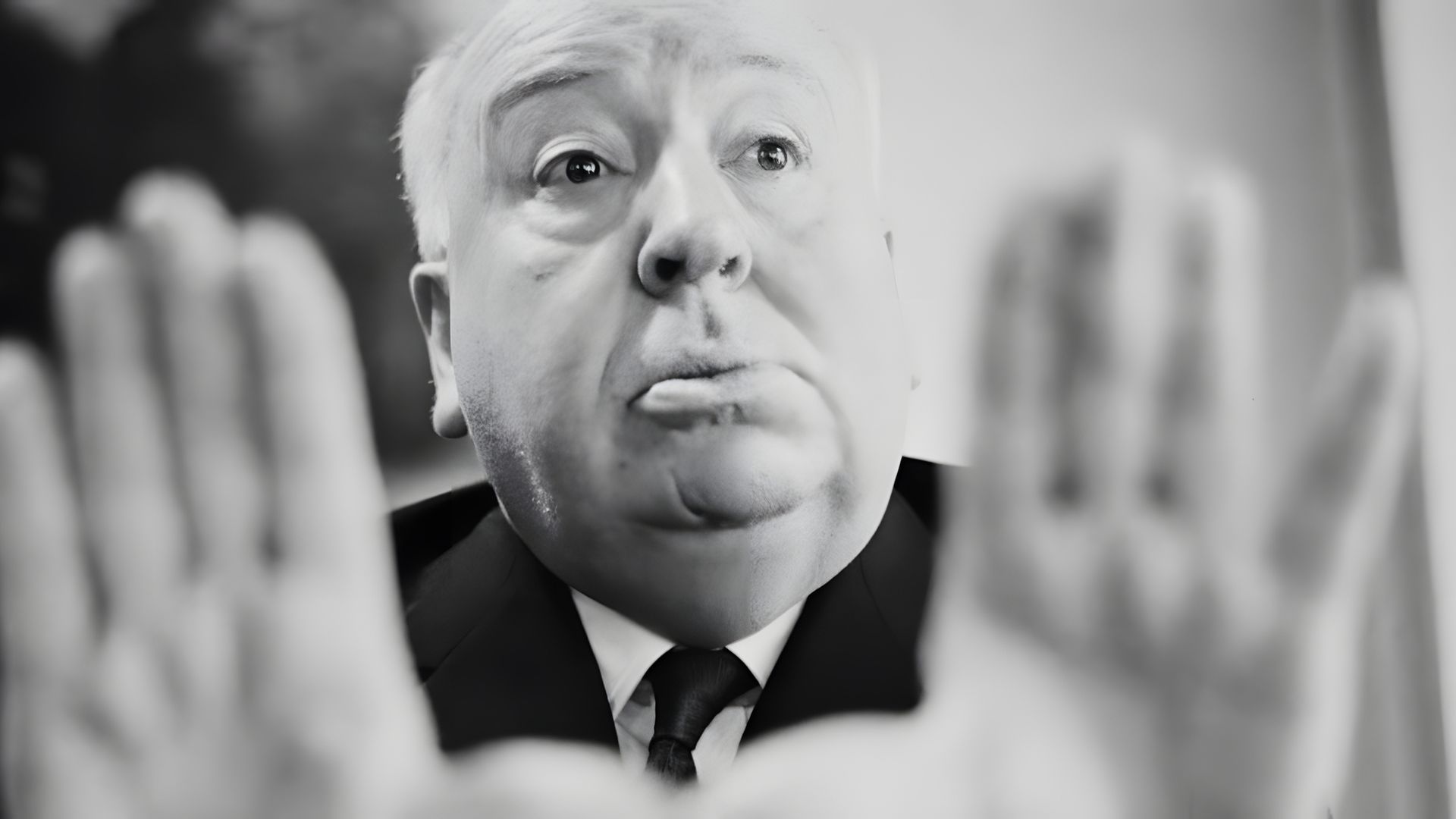 Un primer plano del rostro de Alfred Hitchcock, con las manos extendidas en señal de alto