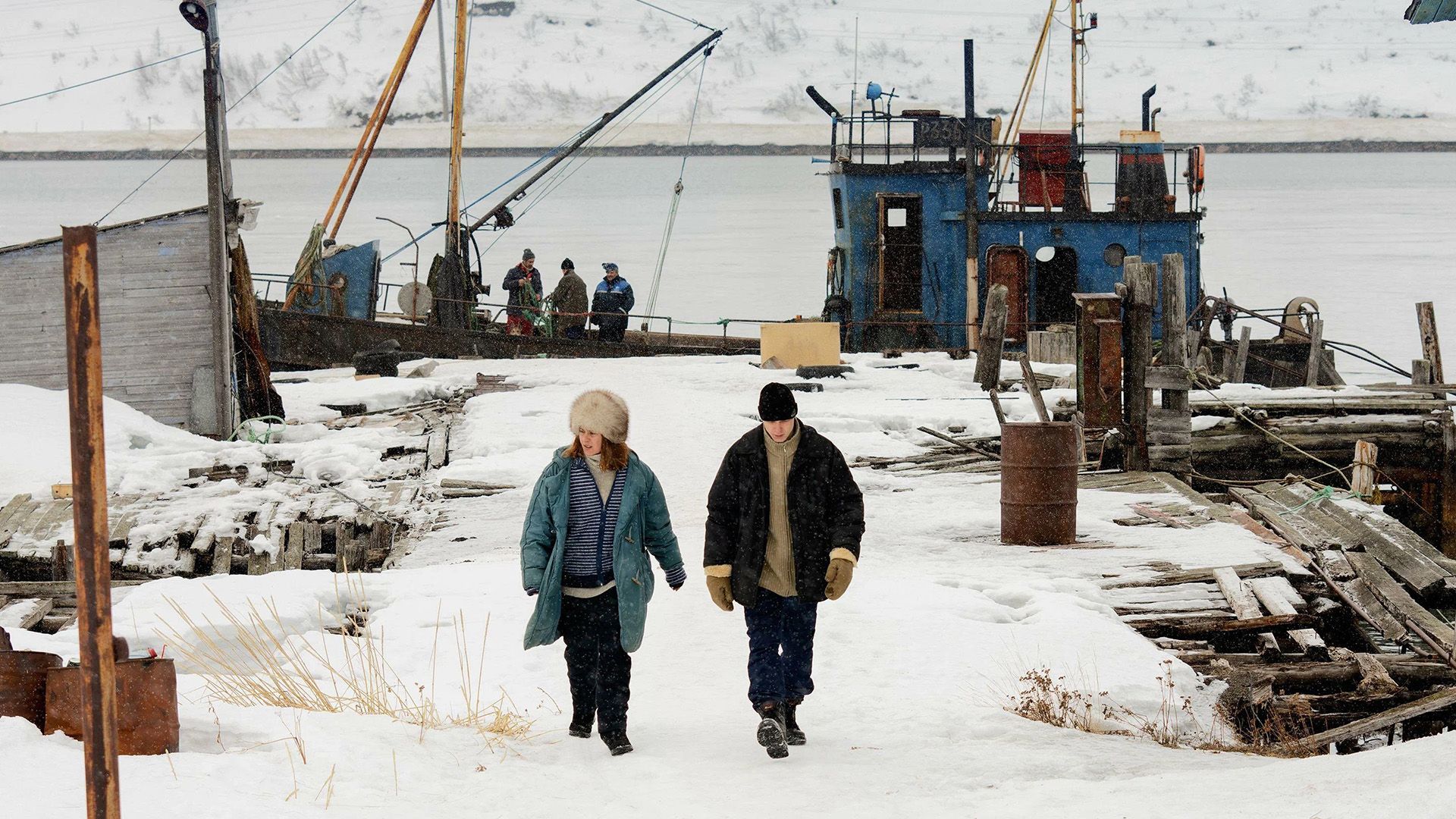 Yura Borisov y Seidi Haarla en una orilla nevada con el telón de fondo de un barco pesquero en una escena de la película "Compartment No. 6"