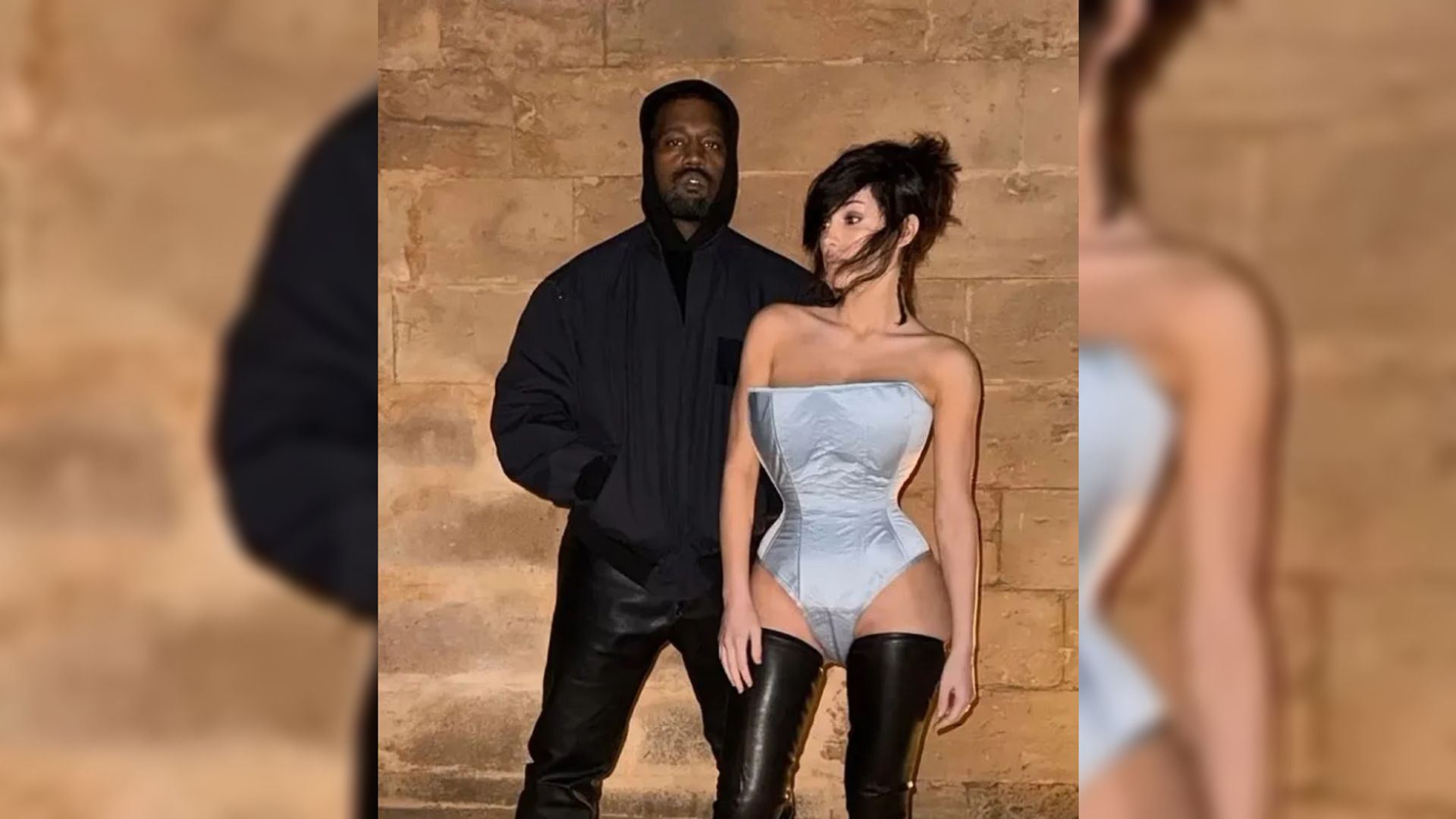 El rapero Kanye West en una chaqueta bomber negra y su esposa Bianca Censori en un bodysuit azul posan contra una pared