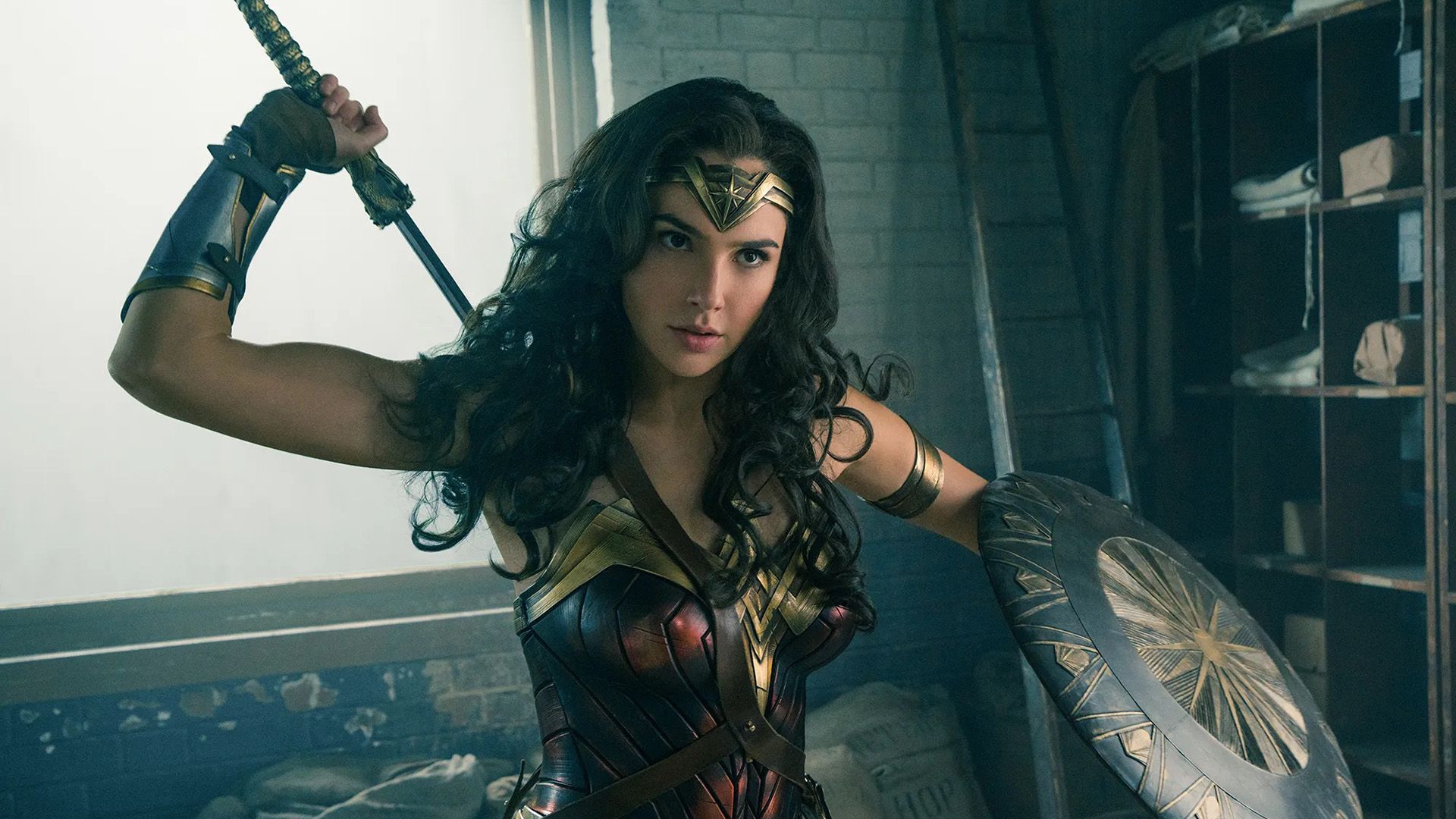 Gal Gadot como Wonder Woman: con armadura, sosteniendo un escudo con su mano izquierda y sacando una espada de detrás de su espalda con su mano derecha