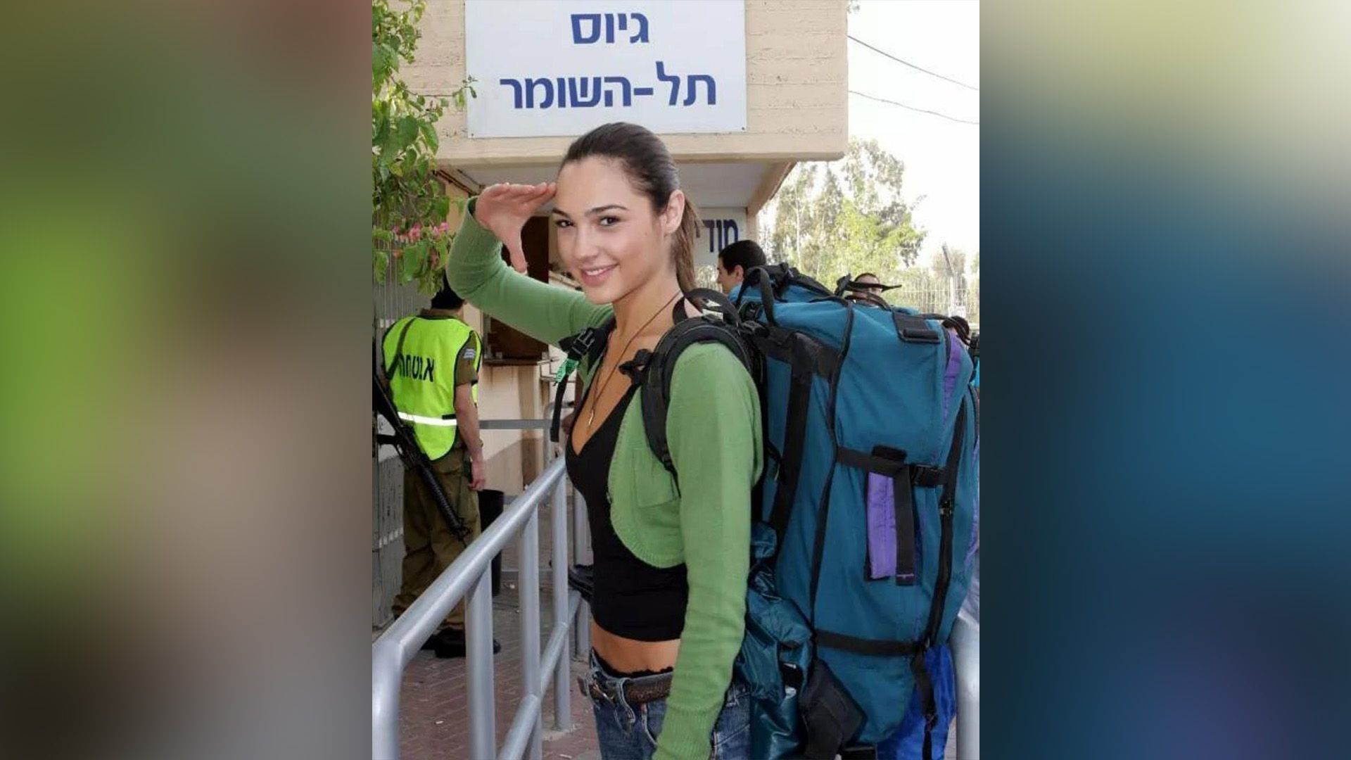 Joven Gal Gadot en un suéter verde y con una gran mochila azul en su espalda saludando con su mano derecha