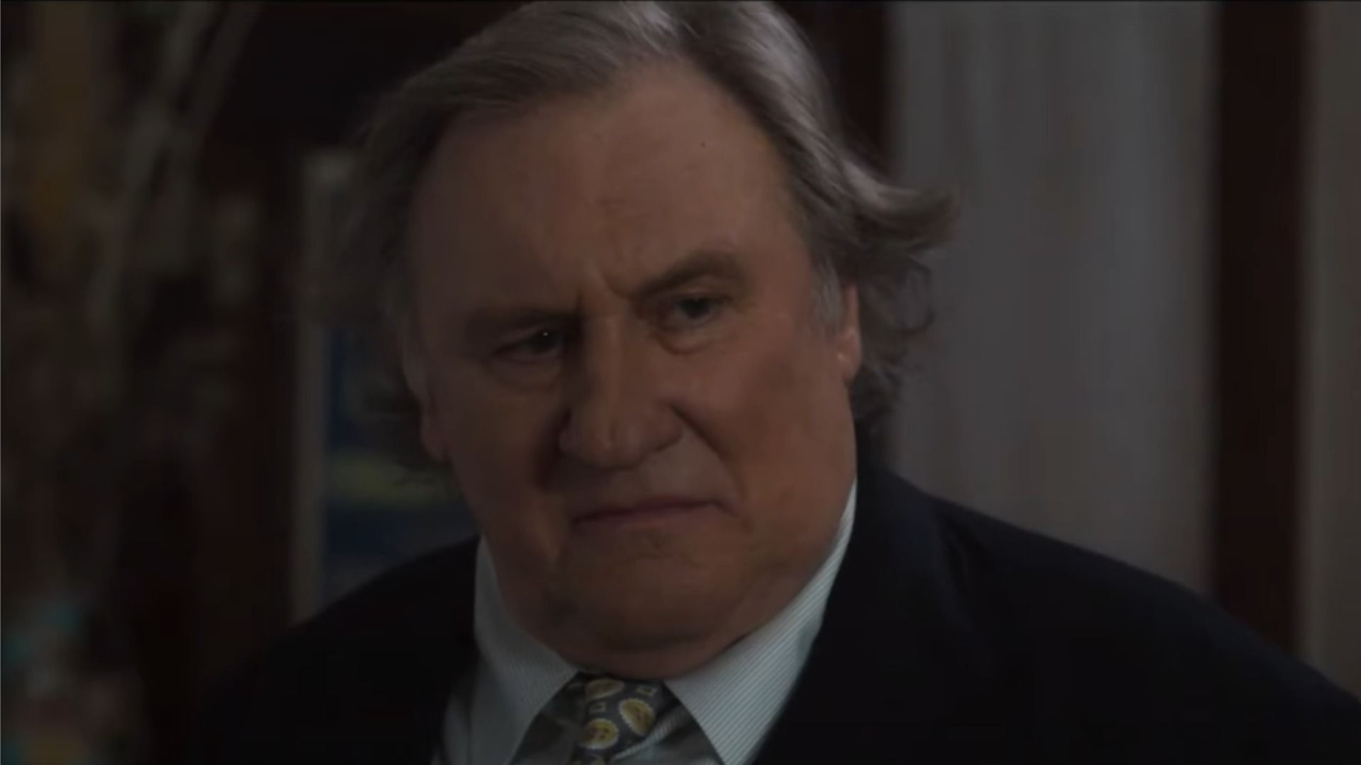 Actor Gérard Depardieu in a classic suit looks sideways against a blurred background