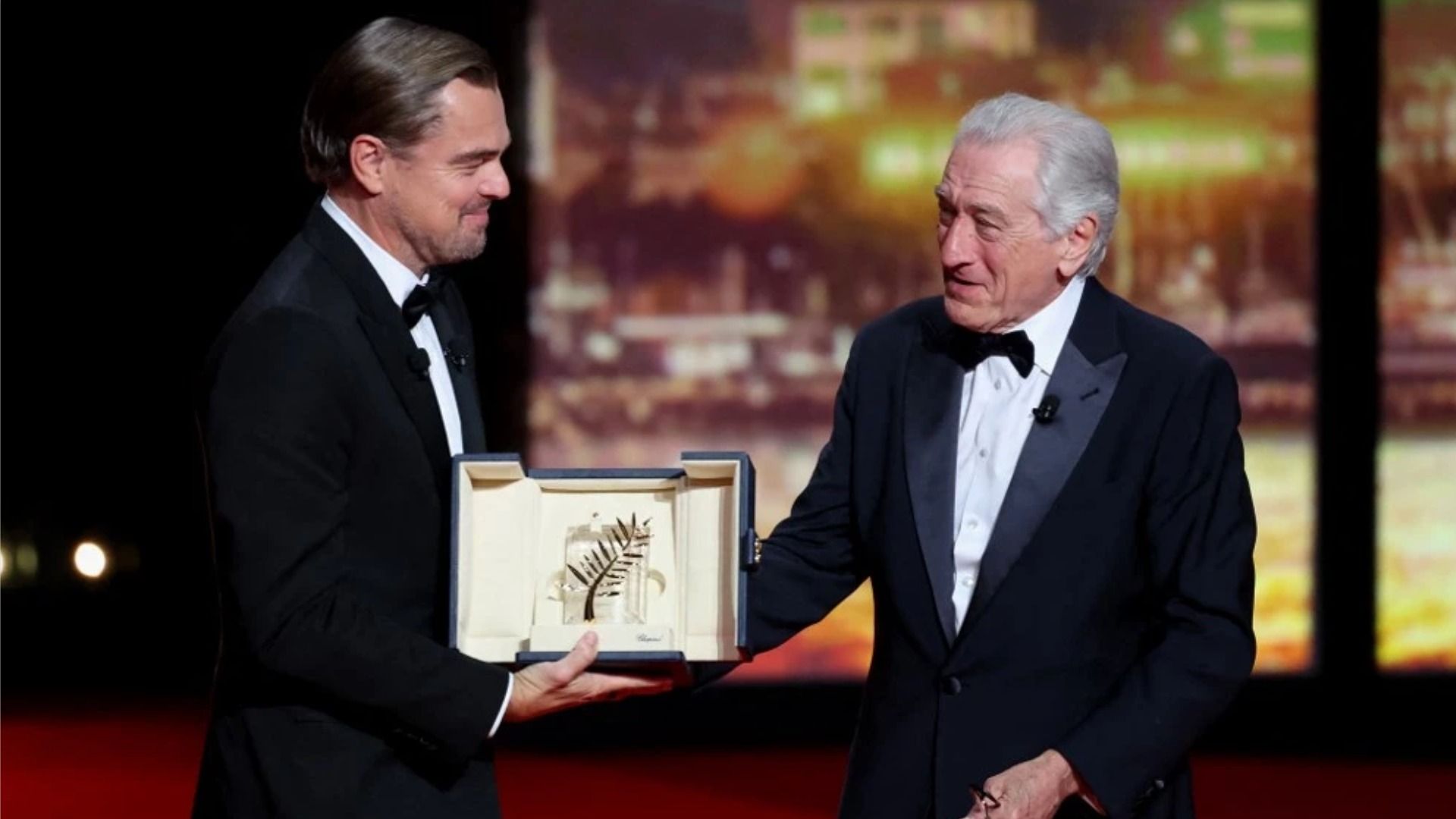 El actor Leonardo DiCaprio sonríe mientras le entrega a Robert De Niro la 'Palme d'Or' en el escenario