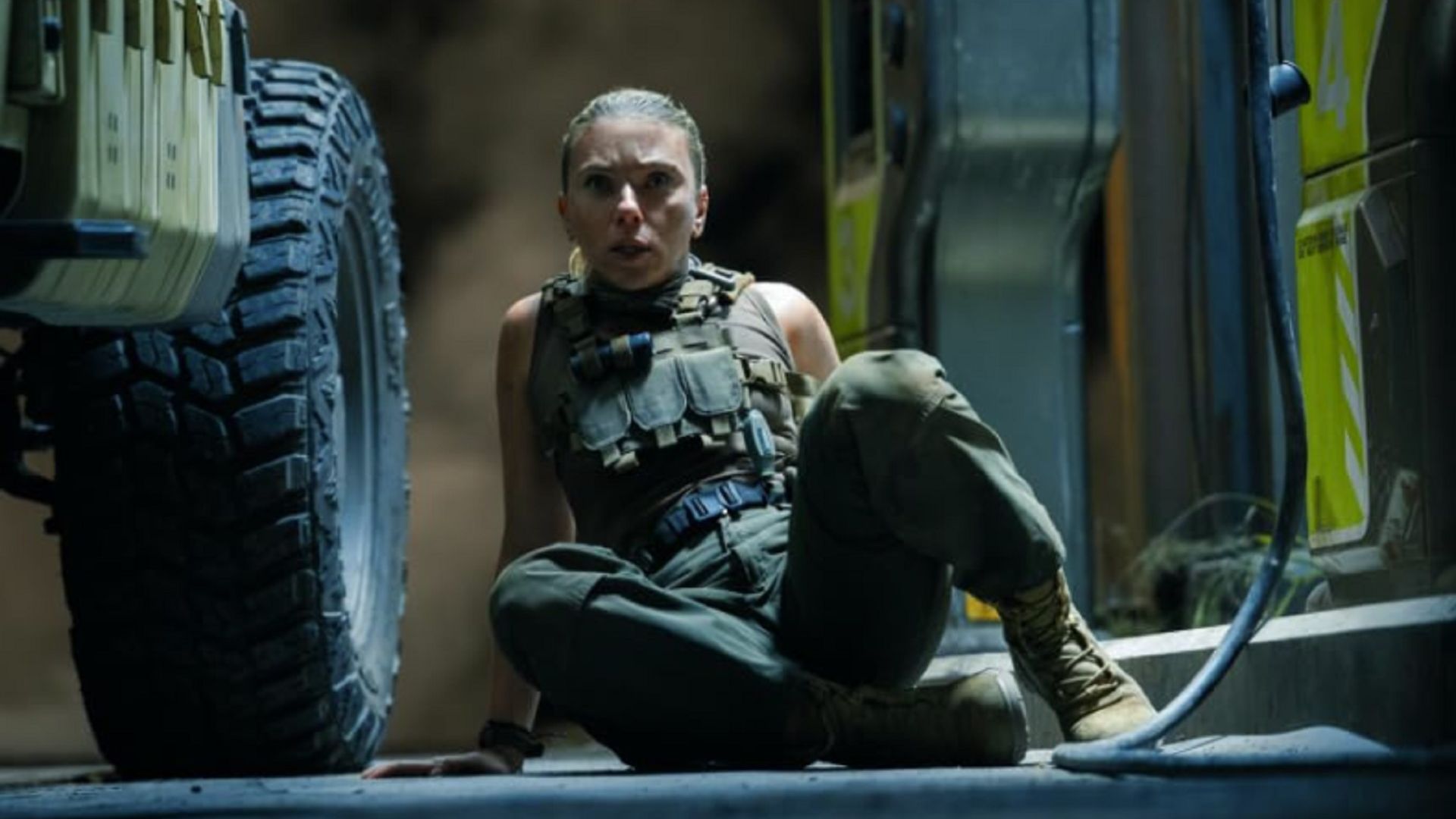 Una asustada Scarlett Johansson sentada en el suelo con un traje de combate