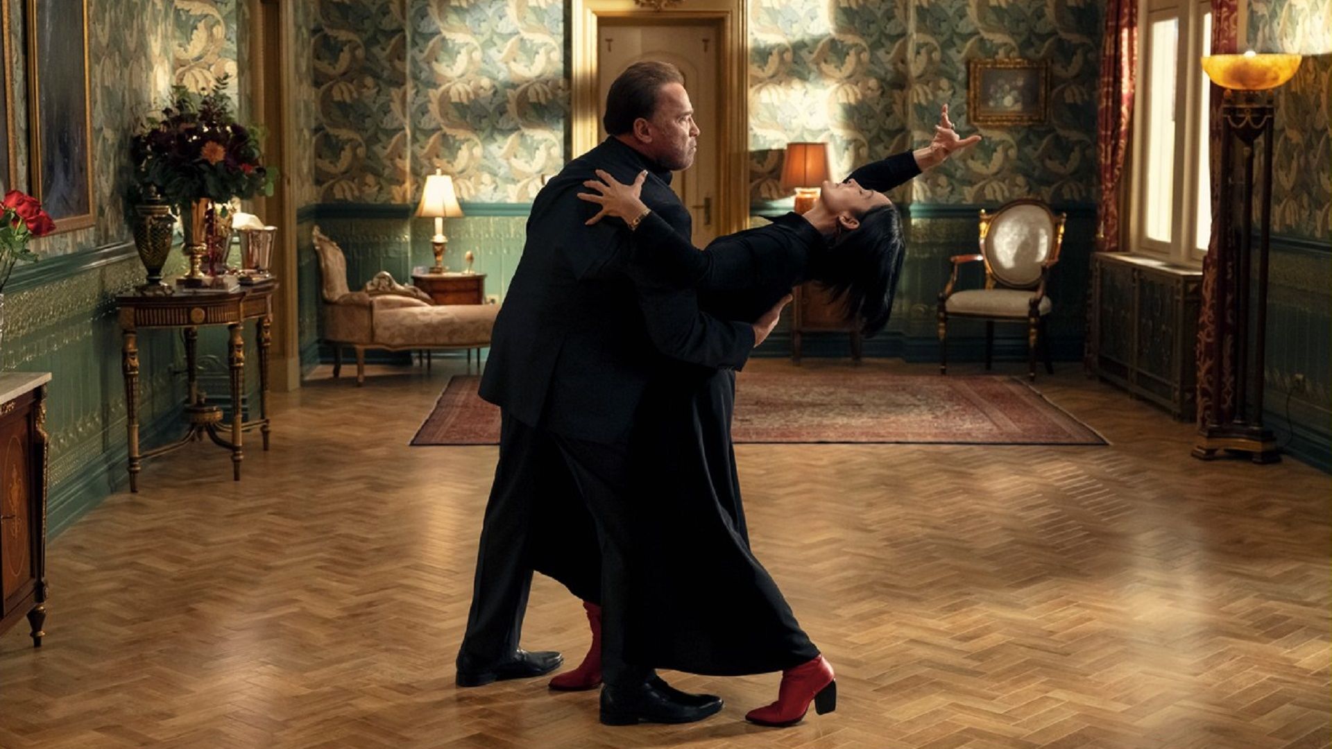 Arnold Schwarzenegger y Carrie-Anne Moss bailando con trajes negros en el medio de la sala
