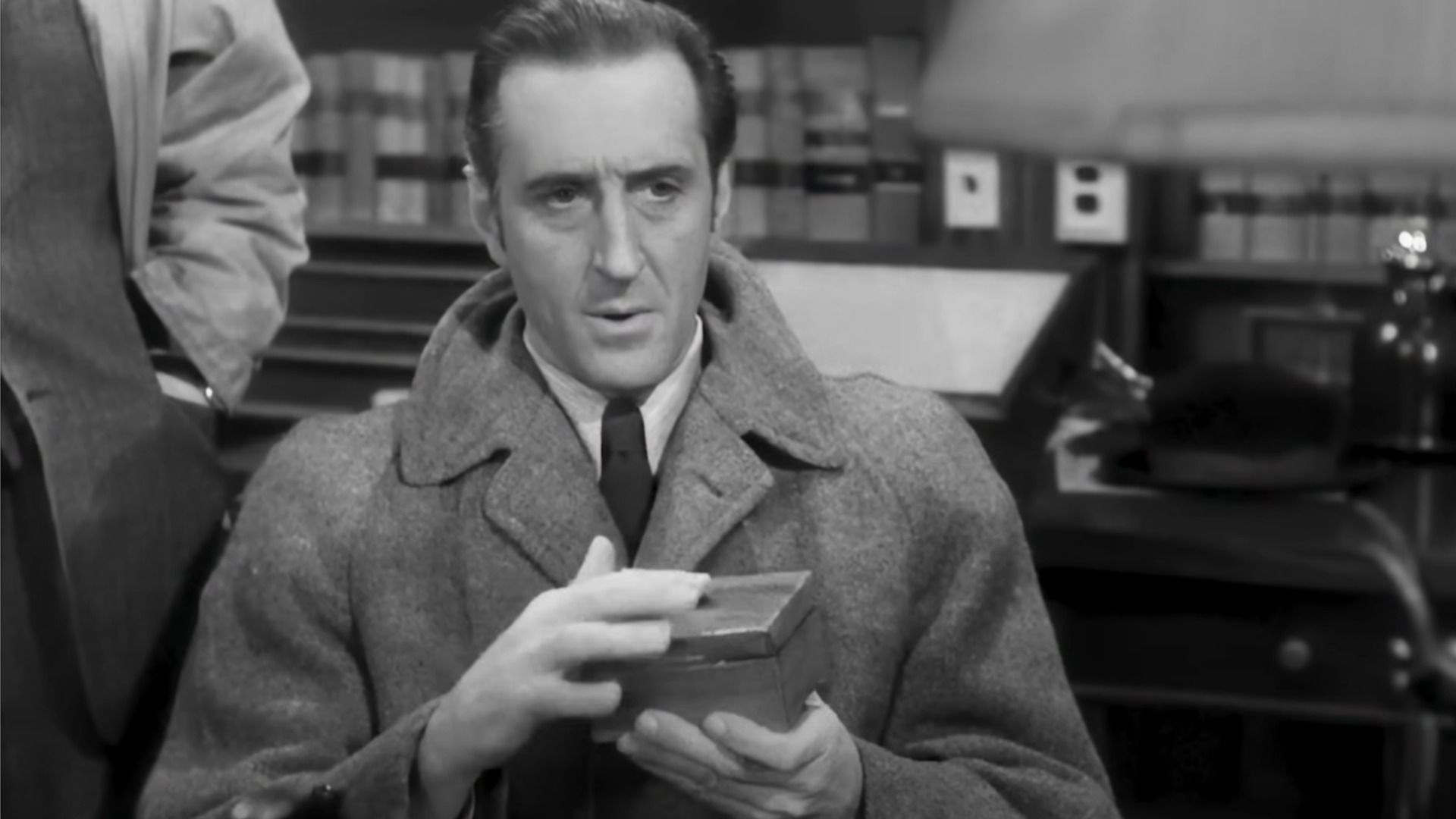 El actor Basil Rathbone como Sherlock Holmes sostiene una caja en sus manos y mira hacia abajo