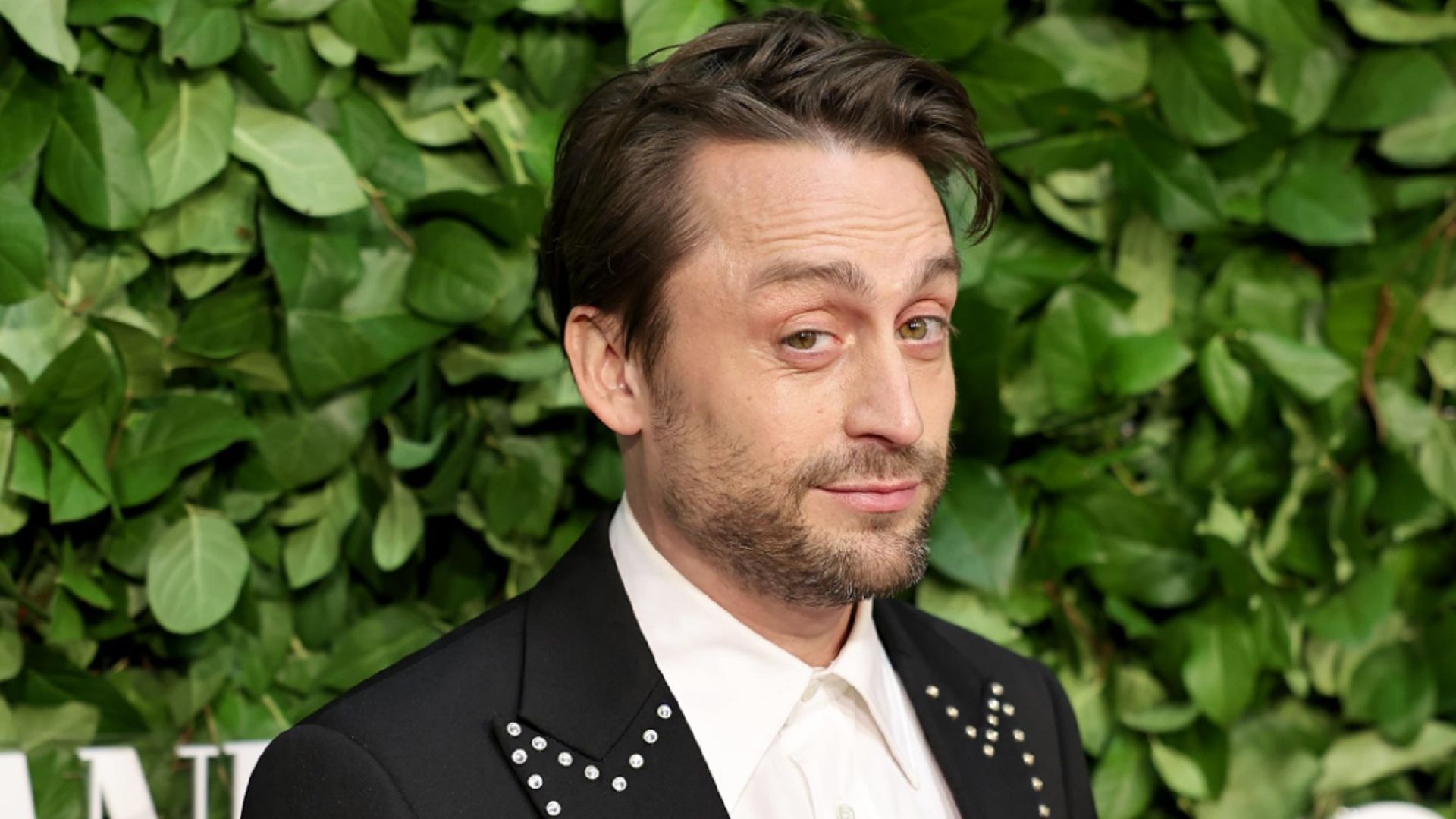 Kieran Culkin mirando irónicamente a la cámara contra una pared de hojas