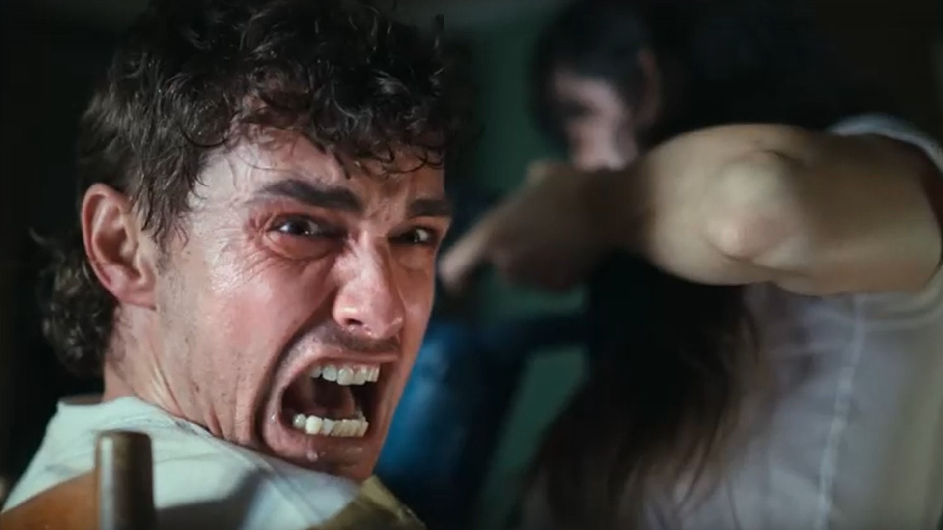 El actor Dave Franco mira hacia un lado y grita mientras está sentado en una silla junto a la actriz Alison Brie