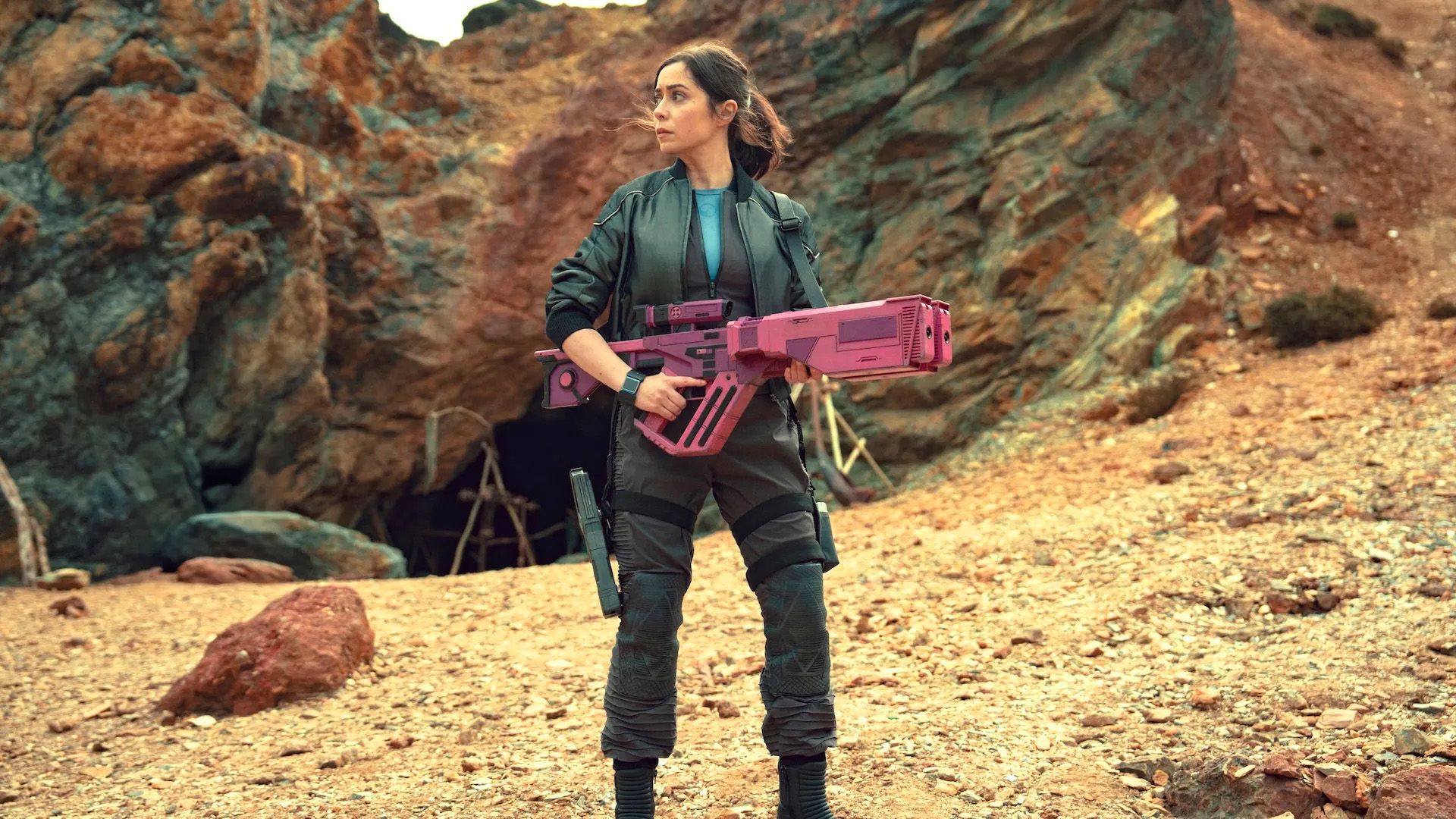 Kristin Milioti sosteniendo un arma futurista rosa en un paisaje desértico