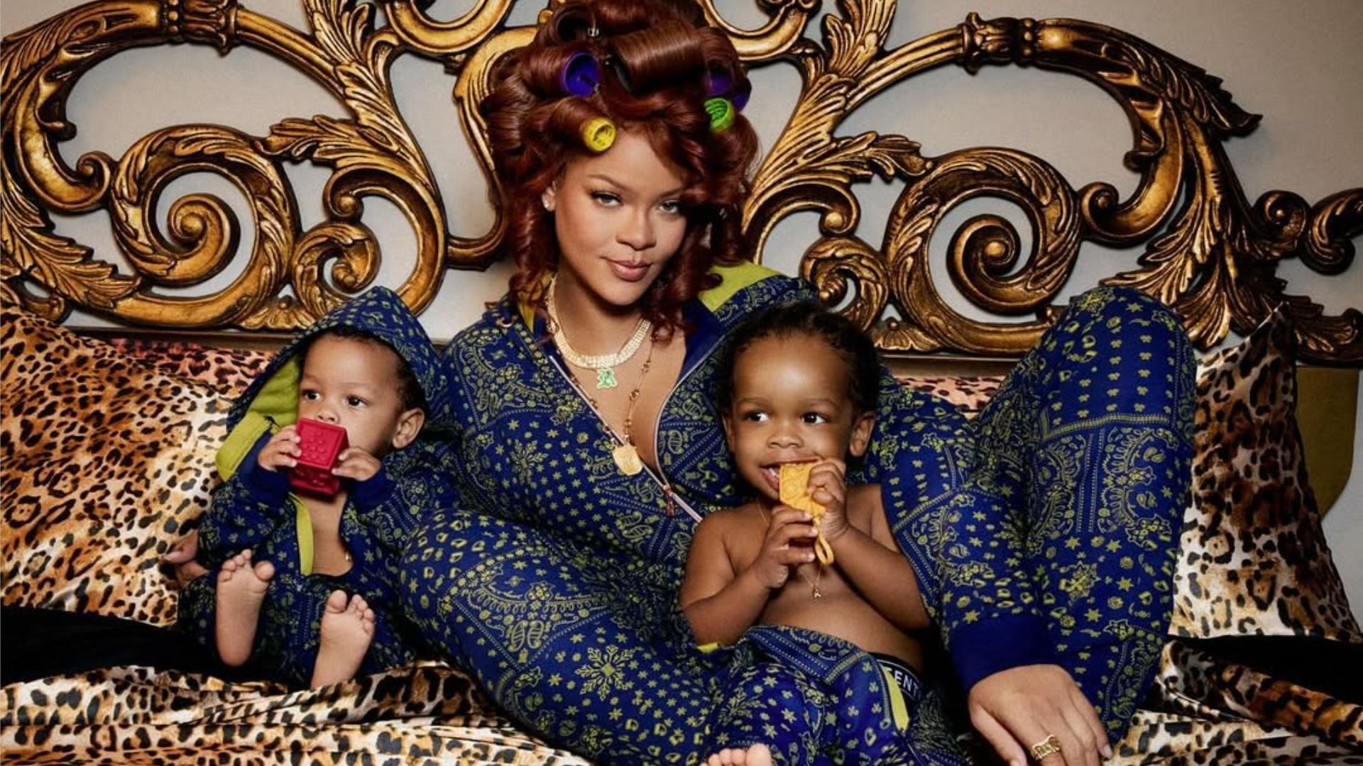 La cantante Rihanna está acostada en la cama con sus hijos RZA y Riot, mirando a la cámara con una sonrisa