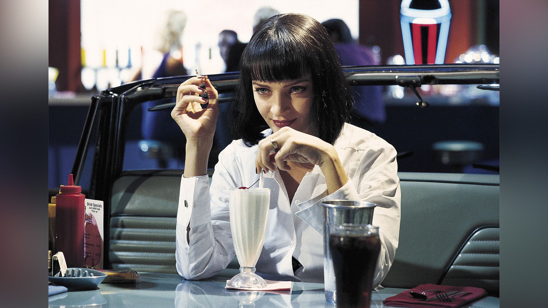 Uma Thurman con una camisa blanca bebiendo un batido en una cafetería en una escena de la película 'Pulp Fiction'