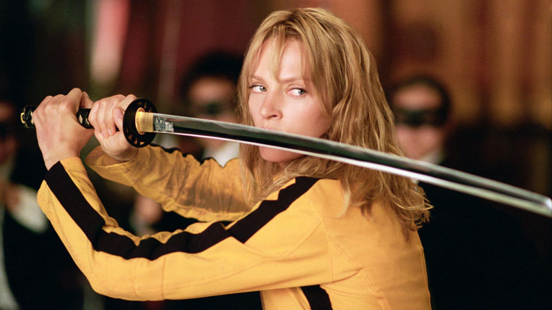 Uma Thurman en un suéter amarillo con rayas negras sostiene una katana frente a su cara en 'Kill Bill'