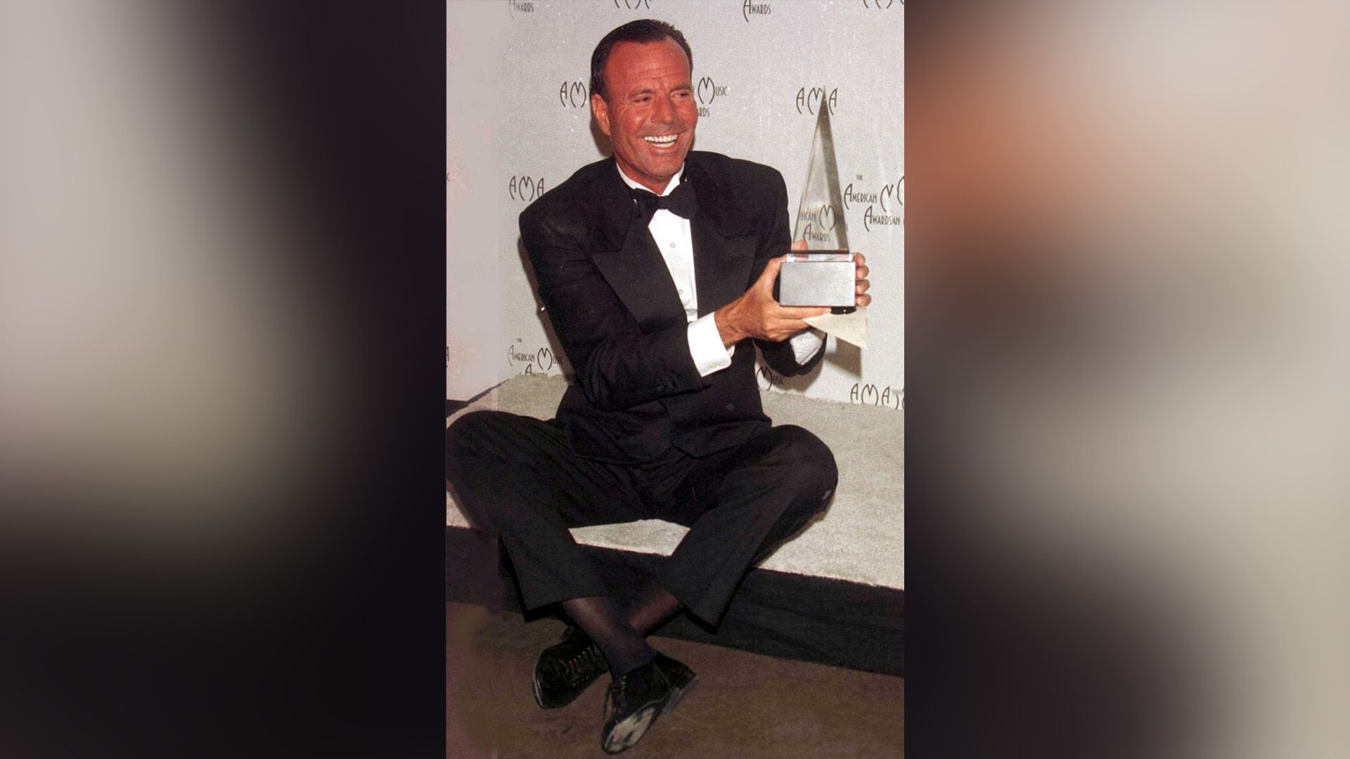 Julio Iglesias feliz en un traje negro sostiene el trofeo de los American Music Awards en sus manos