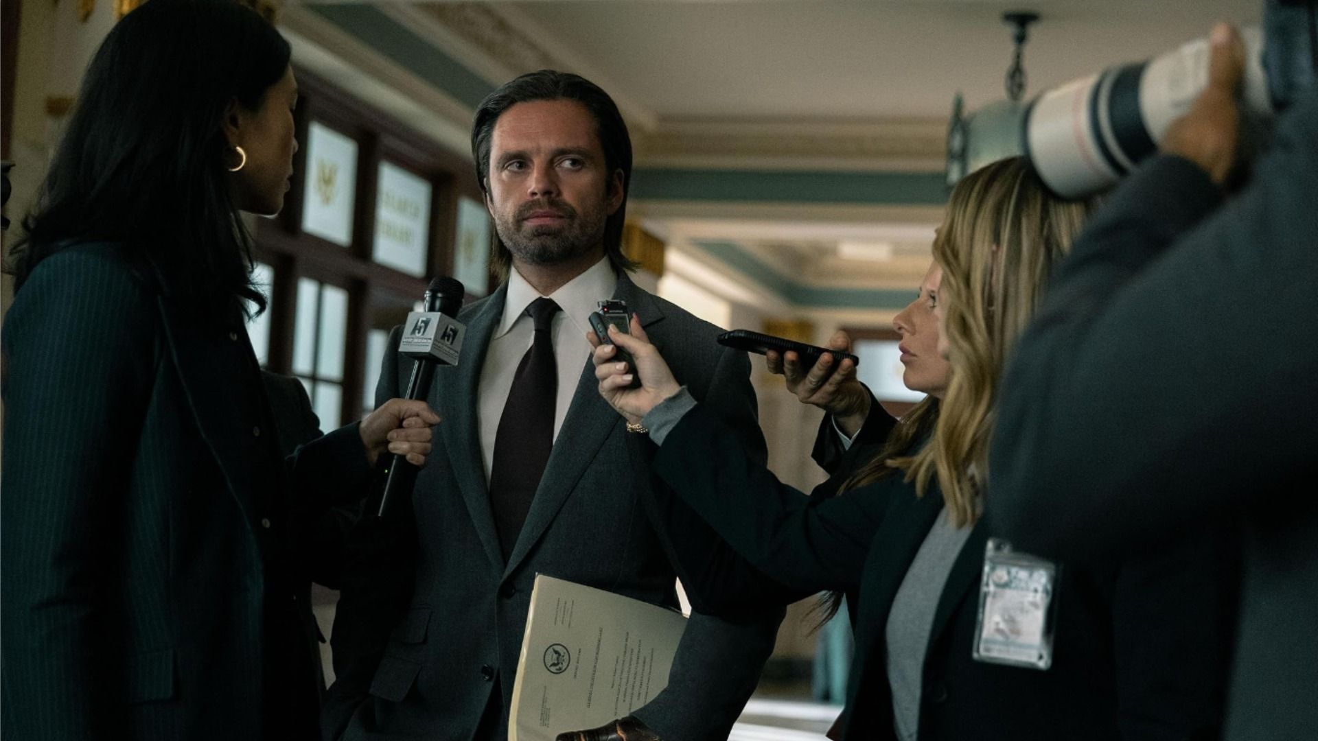 El actor Sebastian Stan con traje negro y cabello largo rodeado de periodistas